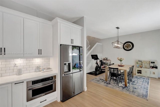 4413 NW 97th Pl, Doral, FL 33178 - kitchen with stainless steel appliances, backsplash, white cabinets, light wood finished floors, and hanging light fixtures