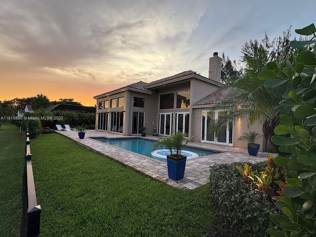 10427 Stonebridge Blvd, Boca Raton, FL 33498 - back of property at dusk with stucco siding, a patio, an outdoor pool, a lawn, and a chimney