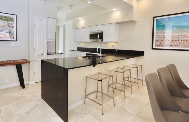 3900 Island Bl Ph 2, Aventura, FL 33160 - kitchen with stainless steel microwave, a sink, white cabinets, a peninsula, and dark countertops