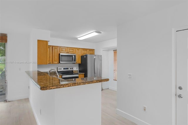 12154 Saint Andrews Pl Unit 112, Miramar, FL 33025 - kitchen with appliances with stainless steel finishes, a peninsula, dark stone counters, baseboards, and light wood-type flooring