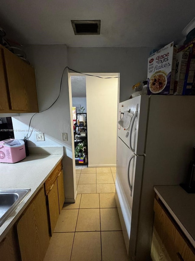 6023 10th Ave N Unit 215, Green Acres, FL 33463 - kitchen featuring brown cabinetry, light tile patterned floors, a sink, light countertops, and freestanding refrigerator