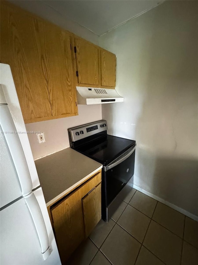 6023 10th Ave N Unit 215, Green Acres, FL 33463 - kitchen featuring under cabinet range hood, electric stove, freestanding refrigerator, dark tile patterned flooring, and brown cabinetry