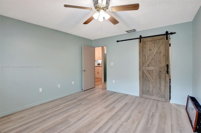 2001 Seagrape Ave, Pembroke Pines, FL 33026 - unfurnished bedroom featuring a barn door, light wood-type flooring, a textured ceiling, ceiling fan, and baseboards