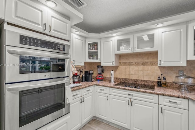 7251 SW 158th Pl, Miami, FL 33193 - kitchen featuring stainless steel double oven, black electric stovetop, white cabinets, tasteful backsplash, and a textured ceiling