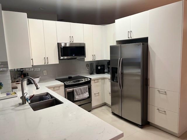 1020 Silktree Ln, Weston, FL 33327 - kitchen featuring appliances with stainless steel finishes, a sink, light countertops, white cabinets, and backsplash
