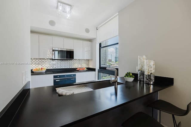 1010 Brickell Ave Unit 1501, Miami, FL 33131 - kitchen with dark countertops, wall oven, tasteful backsplash, white cabinetry, and stainless steel microwave
