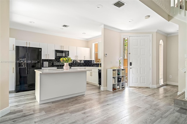 21024 NE 34th Ct, Aventura, FL 33180 - kitchen with black appliances, a kitchen island, ornamental molding, light wood-style floors, and white cabinetry