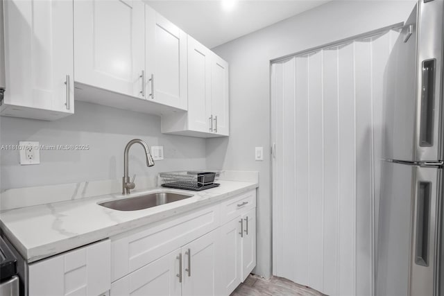 469 NE 207th Ln Unit 205, Miami, FL 33179 - kitchen with freestanding refrigerator, a sink, white cabinetry, light stone counters, and light wood-style floors