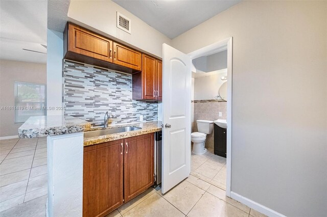 501 Carolina Ave, Fort Lauderdale, FL 33312 - kitchen featuring light tile patterned flooring, a sink, light stone counters, brown cabinetry, and baseboards