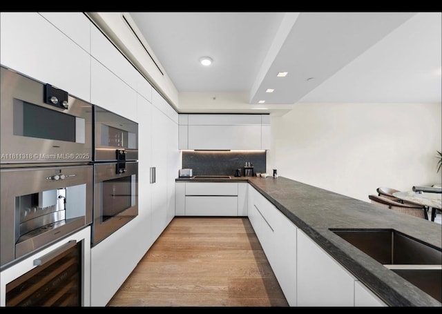 7055 Fisher Island Dr Unit 7055, Miami Beach, FL 33109 - kitchen with white cabinetry, dark countertops, double oven, modern cabinets, and light wood-style flooring