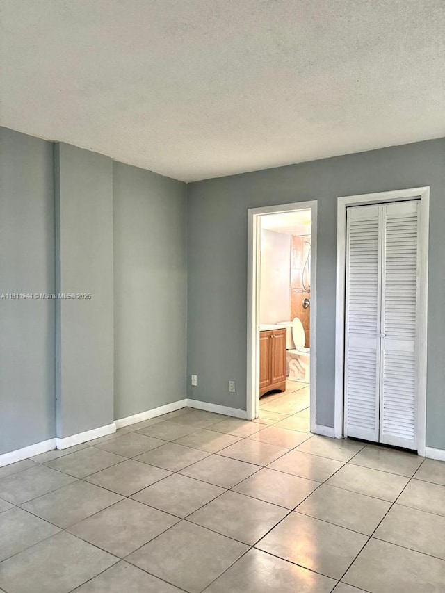 1333 E Hallandale Beach Blvd Unit 134, Hallandale Beach, FL 33009 - unfurnished bedroom featuring light tile patterned floors, a closet, a textured ceiling, baseboards, and connected bathroom