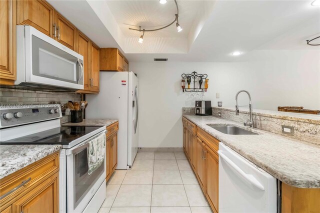 3003 30th Ln, Green Acres, FL 33463 - kitchen featuring white appliances, track lighting, brown cabinetry, backsplash, and a peninsula