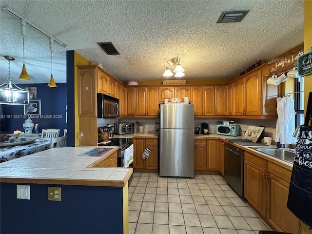 10428 NW 3rd St, Pembroke Pines, FL 33026 - kitchen with appliances with stainless steel finishes, brown cabinetry, light tile patterned floors, a textured ceiling, and a peninsula