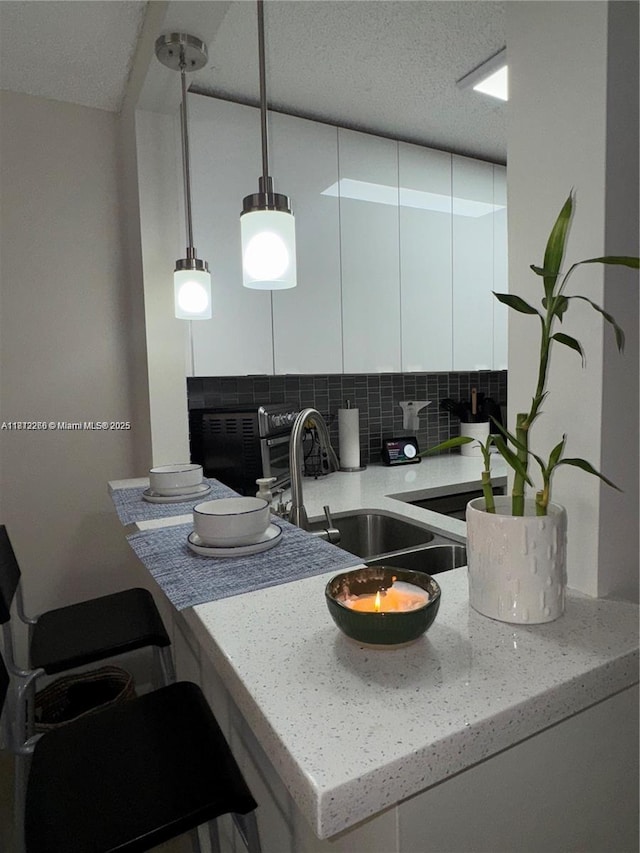 3586 N University Dr Unit U-6, Coral Springs, FL 33065 - kitchen featuring decorative backsplash, white cabinets, a sink, hanging light fixtures, and a peninsula
