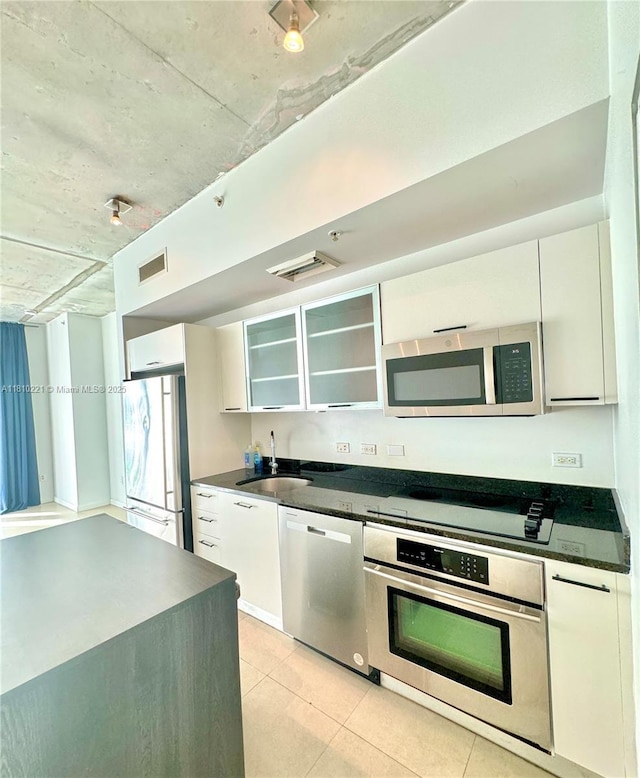 3470 E Coast Ave Unit H1006, Miami, FL 33137 - kitchen with stainless steel appliances, a sink, dark countertops, light tile patterned floors, and glass insert cabinets