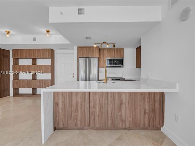4100 Salzedo St Unit 901, Coral Gables, FL 33146 - kitchen with appliances with stainless steel finishes, a peninsula, light countertops, brown cabinets, and a sink