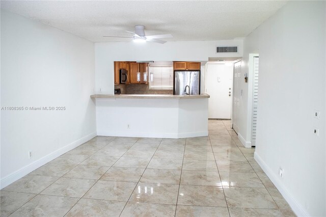 3090 Holiday Springs Blvd Unit 305, Margate, FL 33063 - kitchen featuring stainless steel appliances, brown cabinetry, a ceiling fan, a peninsula, and a textured ceiling
