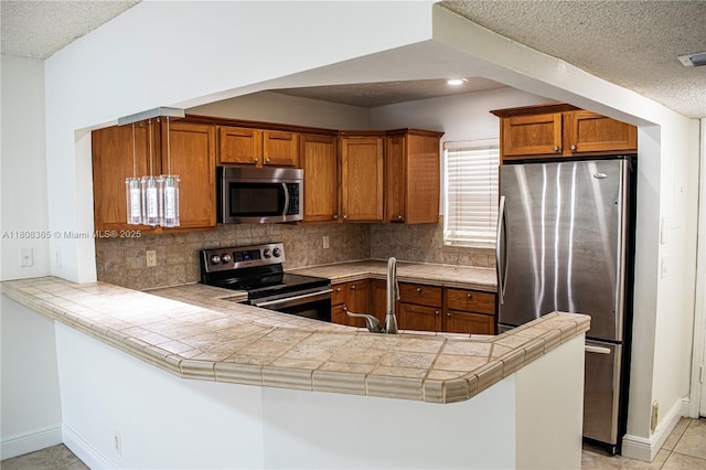 3090 Holiday Springs Blvd Unit 305, Margate, FL 33063 - kitchen featuring stainless steel appliances, brown cabinetry, a textured ceiling, backsplash, and a peninsula