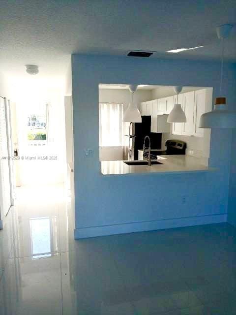 5200 NW 31st Ave Unit 14, Fort Lauderdale, FL 33309 - kitchen featuring a sink, a peninsula, freestanding refrigerator, white cabinetry, and light countertops