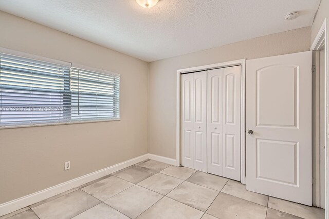 9353 SW 1st Pl, Boca Raton, FL 33428 - unfurnished bedroom with a textured ceiling, a closet, baseboards, and light tile patterned flooring