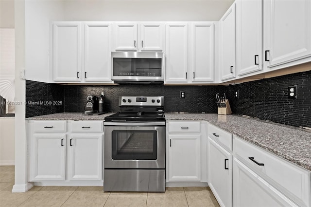 659 NE 191st St, Miami, FL 33179 - kitchen with appliances with stainless steel finishes, light tile patterned floors, white cabinetry, and decorative backsplash