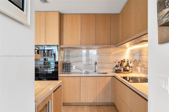 8701 Collins Ave Unit 905, Miami Beach, FL 33154 - kitchen with a sink, black appliances, light countertops, tasteful backsplash, and light wood-type flooring