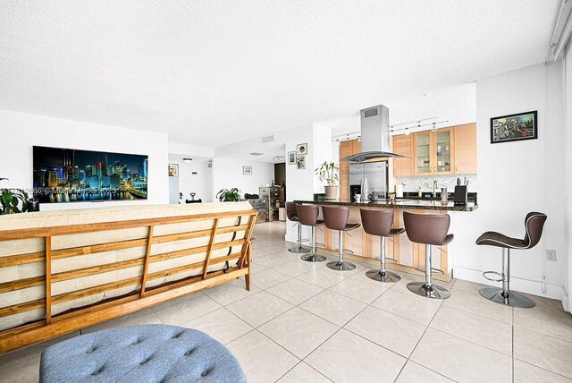 18041 Biscayne Blvd Unit 1201, Aventura, FL 33160 - kitchen with island range hood, a textured ceiling, a breakfast bar area, glass insert cabinets, and light tile patterned floors