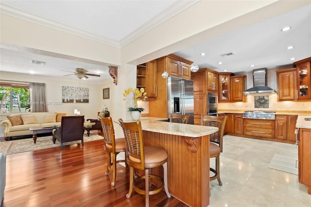 991 Dove Ave, Miami Springs, FL 33166 - kitchen featuring wall chimney range hood, a peninsula, appliances with stainless steel finishes, brown cabinets, and crown molding