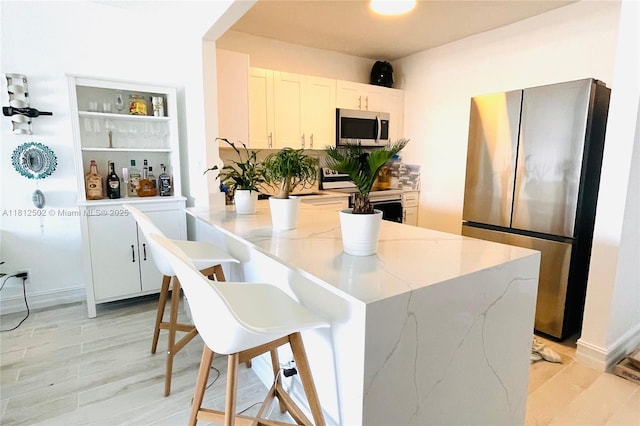 1455 N Treasure Dr Unit 6C, North Bay Village, FL 33141 - kitchen with stainless steel appliances, light stone counters, a kitchen breakfast bar, white cabinets, and light wood finished floors