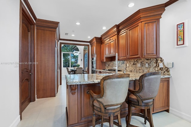 4241 NE 23rd Ter, Lighthouse Point, FL 33064 - kitchen with light stone countertops, a peninsula, tasteful backsplash, a breakfast bar area, and stainless steel double oven