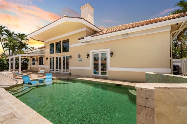 4241 NE 23rd Ter, Lighthouse Point, FL 33064 - back of property at dusk featuring french doors, a patio area, a tiled roof, an outdoor pool, and a chimney