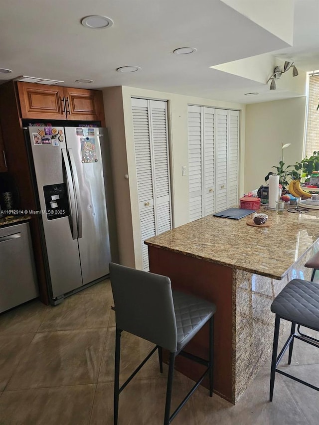 2418 NE 10th St Unit 127, Hallandale Beach, FL 33009 - kitchen with stainless steel fridge, a kitchen bar, brown cabinetry, light stone countertops, and recessed lighting