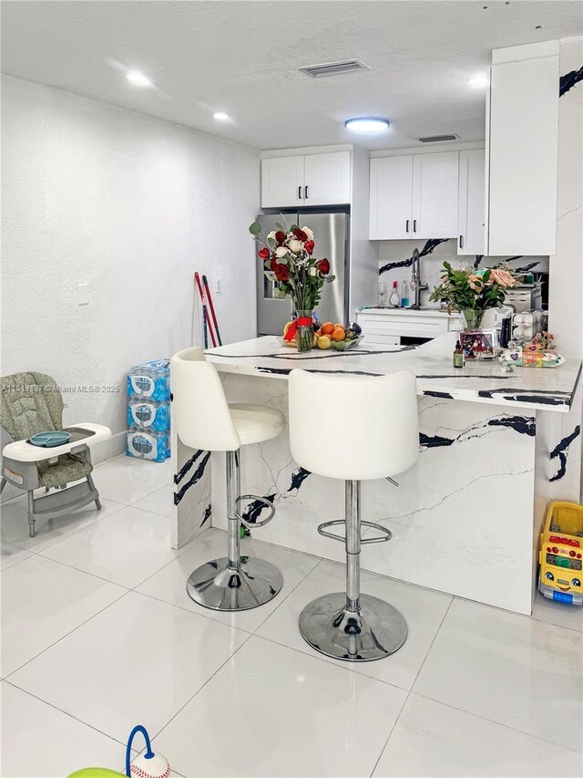 350 W 16th St, Hialeah, FL 33010 - kitchen featuring freestanding refrigerator, white cabinetry, a kitchen breakfast bar, a peninsula, and tile patterned floors