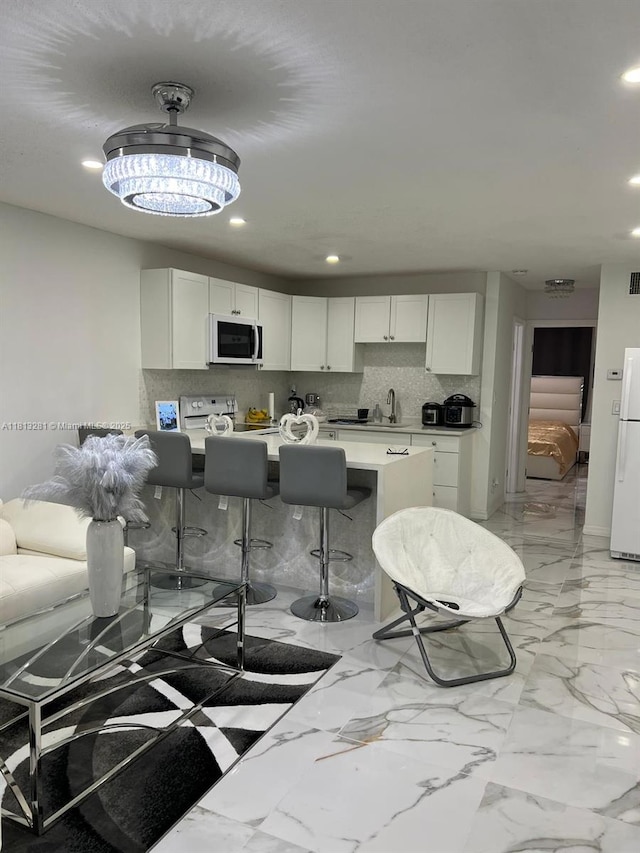 2905 Pierce St Unit 7, Hollywood, FL 33020 - kitchen featuring white appliances, recessed lighting, white cabinets, light marble finish floors, and a kitchen breakfast bar