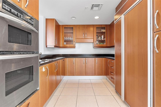 19400 Turnberry Way Unit 1131, Aventura, FL 33180 - kitchen featuring stainless steel double oven, brown cabinets, light tile patterned floors, dark countertops, and glass insert cabinets