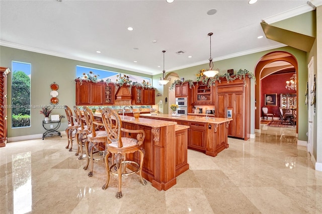 3308 Islewood Ave, Weston, FL 33332 - kitchen with arched walkways, a large island, brown cabinetry, a breakfast bar area, and ornamental molding