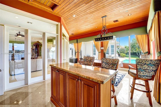 3308 Islewood Ave, Weston, FL 33332 - kitchen with wooden ceiling, light stone counters, decorative light fixtures, brown cabinets, and a center island