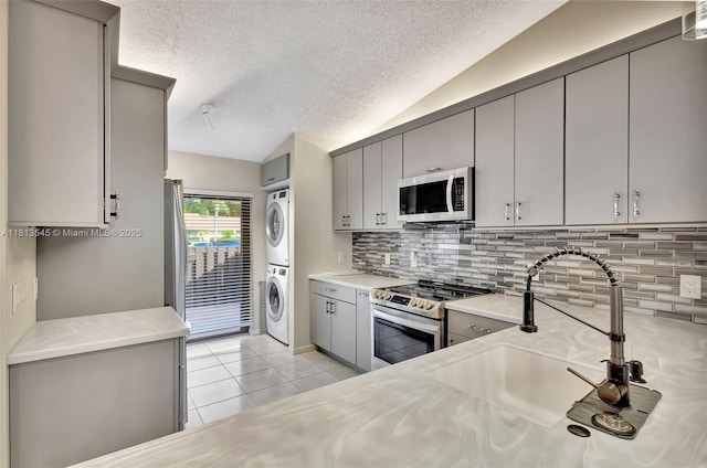 4864 Sable Pine Cir Unit A, West Palm Beach, FL 33417 - kitchen featuring appliances with stainless steel finishes, estacked washer and dryer, gray cabinets, lofted ceiling, and a textured ceiling