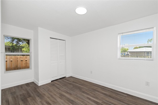 2374 NW 56th St, Miami, FL 33142 - unfurnished bedroom featuring dark wood-type flooring, multiple windows, baseboards, and a closet
