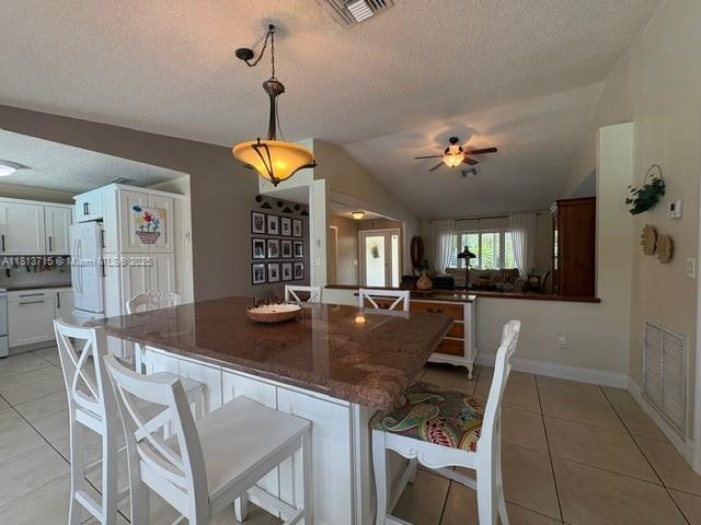 13324 SW 100th Ter, Miami, FL 33186 - kitchen featuring freestanding refrigerator, a textured ceiling, light tile patterned floors, a breakfast bar area, and vaulted ceiling
