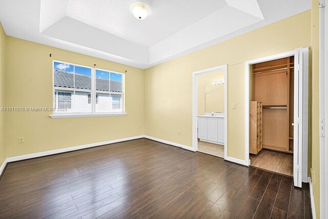 5440NW 107th Ave Unit 204, Doral, FL 33178 - unfurnished bedroom featuring a tray ceiling, dark wood-style flooring, baseboards, a closet, and ensuite bathroom
