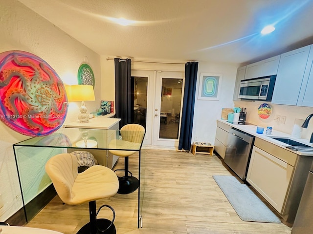 928 NE 18th Ct, Fort Lauderdale, FL 33305 - kitchen with stainless steel appliances, french doors, a sink, light wood finished floors, and light countertops