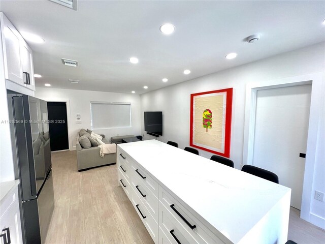 1451 NE 155th Ter, North Miami Beach, FL 33162 - kitchen featuring light wood-style flooring, white cabinetry, open floor plan, a center island, and light countertops