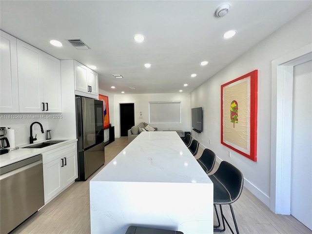 1451 NE 155th Ter, North Miami Beach, FL 33162 - kitchen featuring stainless steel appliances, a sink, a center island, light wood-style floors, and white cabinets