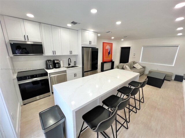 1451 NE 155th Ter, North Miami Beach, FL 33162 - kitchen with appliances with stainless steel finishes, a sink, a center island, a breakfast bar area, and white cabinetry