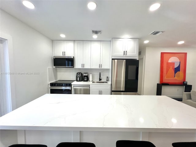 1451 NE 155th Ter, North Miami Beach, FL 33162 - kitchen featuring stainless steel appliances, a sink, a breakfast bar, white cabinets, and recessed lighting