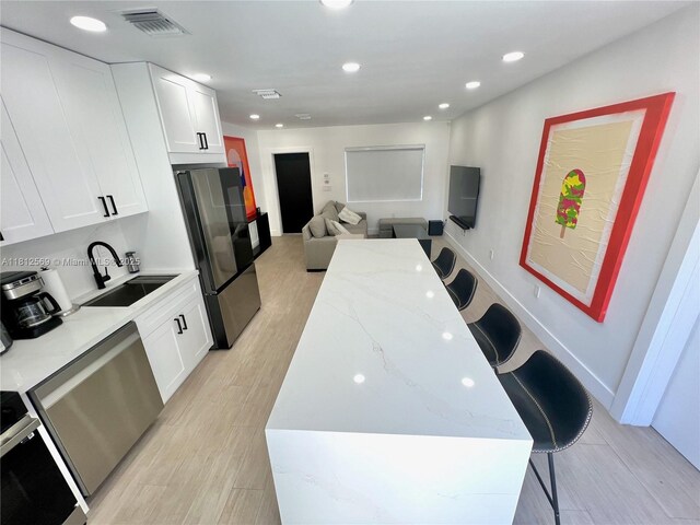 1451 NE 155th Ter, North Miami Beach, FL 33162 - kitchen with stainless steel appliances, a sink, light stone countertops, white cabinets, and light wood-style flooring