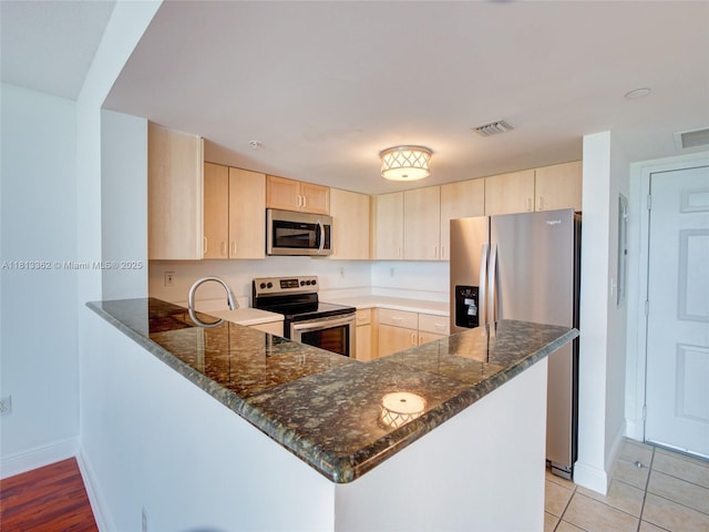 3000 Coral Way Unit 715, Miami, FL 33145 - kitchen featuring appliances with stainless steel finishes, light brown cabinetry, a peninsula, dark stone countertops, and light tile patterned floors