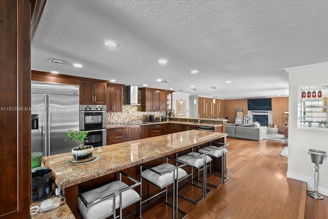 3030 SW 117th Ave, Davie, FL 33330 - kitchen with wall chimney range hood, appliances with stainless steel finishes, a sink, wood finished floors, and a breakfast bar