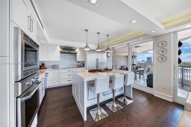 2901 S Bayshore Dr Unit 17G/H, Miami, FL 33133 - kitchen featuring appliances with stainless steel finishes, exhaust hood, white cabinetry, light stone counters, and backsplash